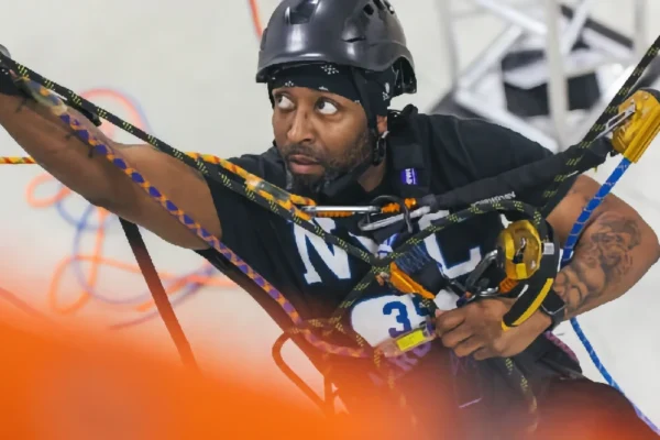 A man wearing a helmet and harness handles multiple climbing ropes during an indoor rope access or safety training exercise.