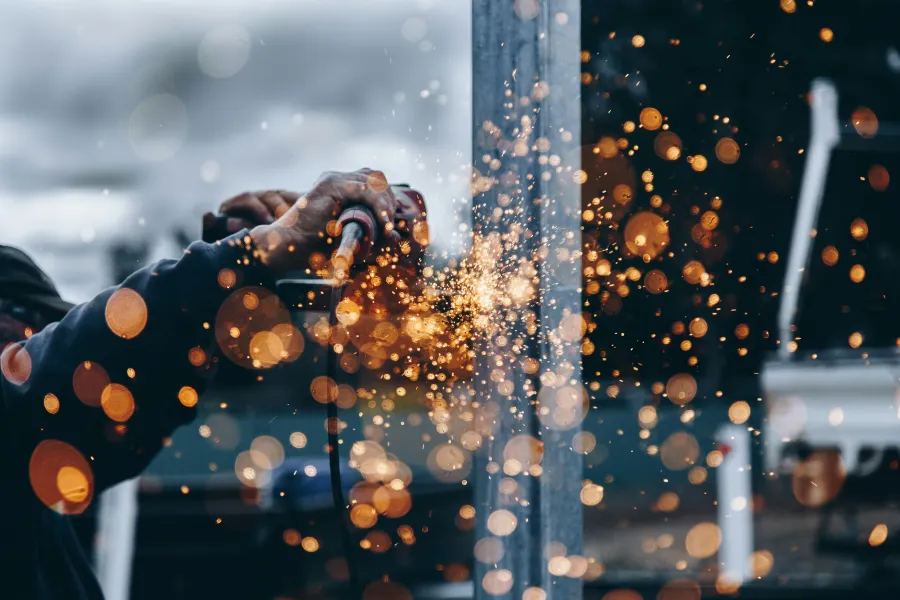 Person using a power tool to grind metal, creating bright orange sparks that scatter in front of a blurred background.